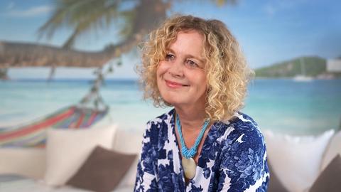 Potrait Karen Wittel, die vor einer Fototapete mit Strandmotiv sitzt.