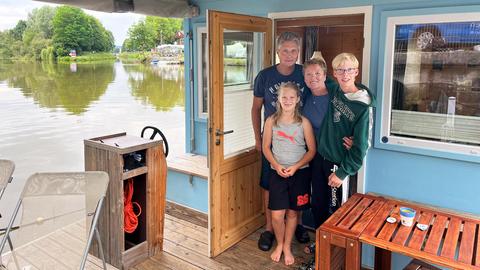 Foto von einer Frau, einem Mann und zwei Kindern, die in der Tür eines Hausbootes stehen. Im Hintergrund ein Fluss und ein Ufer.