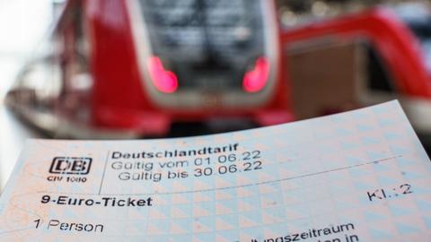 Ein 9-Euro-Ticket in Papierform - scharf im Bildvordergrund. Züge im Bahnhof unscharf im Bildhintergrund.