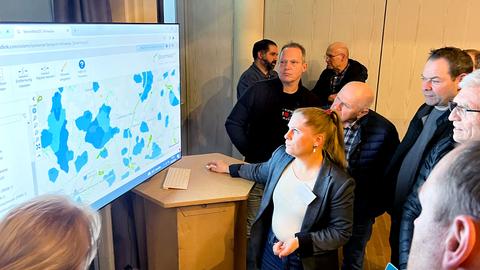 Foto: Eine Gruppe von Menschen stehen vor einem großen Computerbildschirm auf dem eine Karte zu sehen ist.