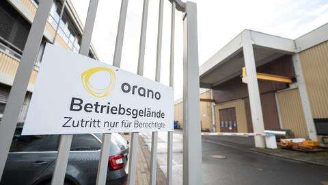 Blick durch ein Eingangstor mit der Aufschrift "Orano" auf einen Parkplatz und mehrere Firmengebäude.