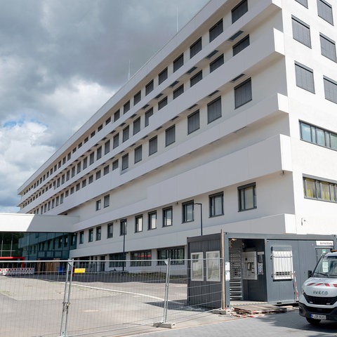 Mehrgeschossiges, weißes Gebäude mit Bauzaun und Handwerkerauto daneben.