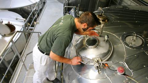 Ein Bierbrauer guckt von oben in einen Kessel. Daneben stehen weitere Kessel.