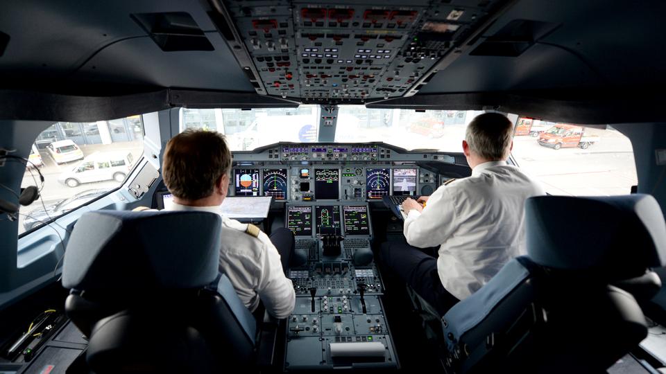 Zwei Piloten von hinten wie sie in einem Cockpit eines Flugzeuges sitzen.