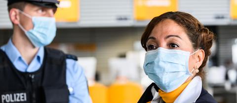 Ein Polizist und eine Polizistin mit OP-Masken in einer Flughafenhalle.