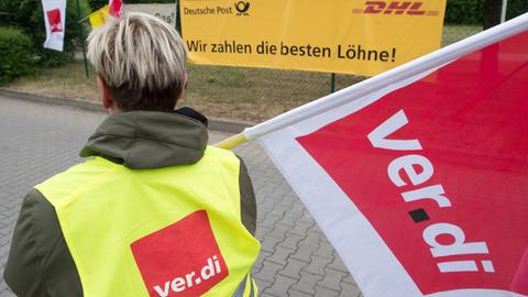 Eine Frau mit Verdi-Flagge vor einem Post-Plakat.