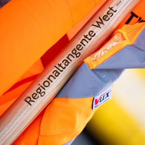 Spatenstiel mit der Aufschrift Regionaltangente West – der Spaten liegt auf einer orangefarbenen Warnweste