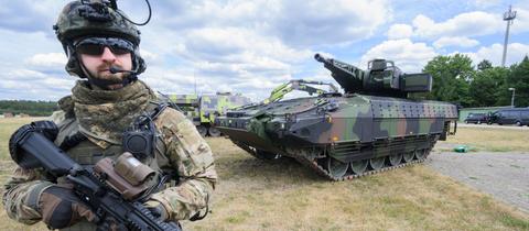 Der Schützenpanzer Puma auf dem Rheinmetall-Werksgelände in Unterlüß, davor steht ein Mann in Soldatenuniform und mit Maschinengewehr