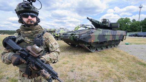 Der Schützenpanzer Puma auf dem Rheinmetall-Werksgelände in Unterlüß, davor steht ein Mann in Soldatenuniform und mit Maschinengewehr