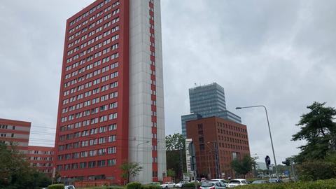 Ein rot-weiß gestrichenes Hochhaus, im Vordergrund parkende Autos an einer Straße.