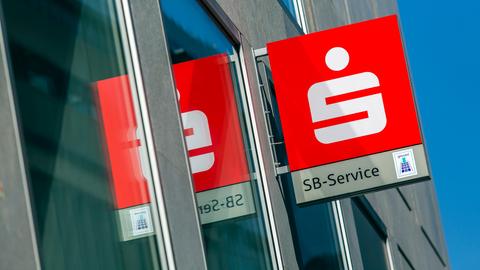 Ein Leuchtschild eines Sparkasse SB-Service an einer Fassade spiegelt sich in der Glasfläche.