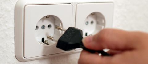Steckdose in einer Wand, in welche eine Hand einen Netzstecker steckt.