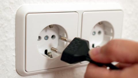 Steckdose in einer Wand, in welche eine Hand einen Netzstecker steckt.