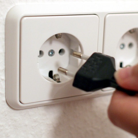 Steckdose in einer Wand, in welche eine Hand einen Netzstecker steckt.