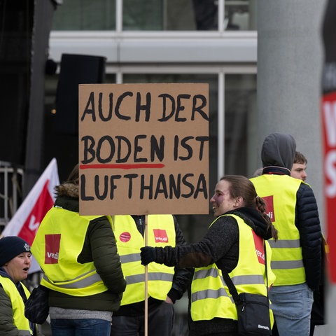 "Auch der Boden ist Lufthansa" steht auf einem Plakat, mit dem sich eine Frau am Streik beteiligt.
