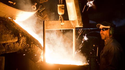 Gießerei eines Autozuliefer-Betriebs - ein Mann in Schutzkleidung neben Kessel mit flüssigem Stahl