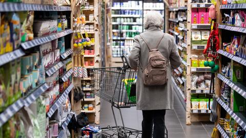 Eine Frau geht mit ihrem Einkaufswagen zwischen Regalen durch einen Supermarkt.