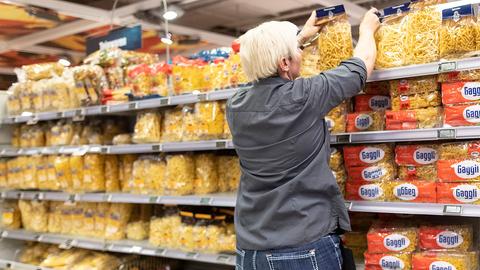 Eine Supermarkt-Mitarbeiterin füllt ein Regal mit Nudeln auf. 