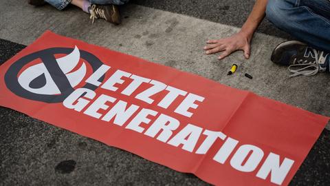 Ein Aktivist der Gruppe "Letzte Generation", der seine Hand selbst auf der Straße festgeklebt hat, blockiert eine Kreuzung in Göttingen.