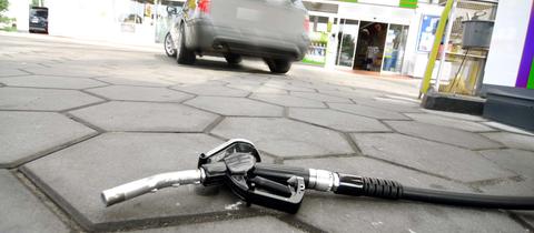 Zapfhahn einer Tankstelle liegt auf dem Boden, Fahrzeug entfernt sich schnell.