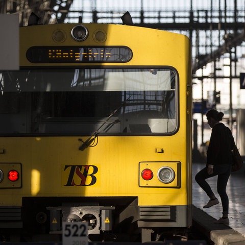 Ein gelber Zug der Taunusbahn steht am Prellbock im Frankfurter Hauptbahnhof. Rechts davon ist die Silouette einer Frau zu erkennen, die in die Bahn einsteigt.