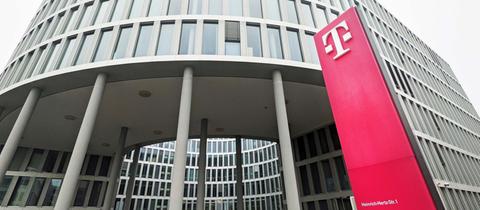 Bürogebäude der Telekom in Darmstadt. Vor dem Gebäude ragt eine magenatfarbene Stele mit dem Telekom-Logo in die Höhe.