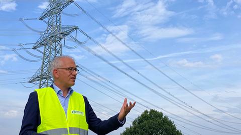 Ein Mann in einer gelben Weste steht vor einem Strommast.