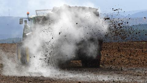 Dampfender Stallmist wird mit landwirtschaftlichem Gerät auf einem Feld ausgebracht. Stallmist ist Dünger und reich an Nährstoffen.