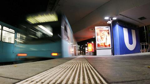 Foto aus der Froschperspektive vom Boden einer U-Bahn-Station. Links eine fahrende U-Bahn (unscharf), rechts ein Betonpfeiler, auf welchem ein großes "U" zu sehen ist.