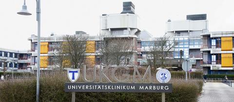 Außenansicht des Gebäudes der Universitätsklinik auf den Marburger Lahnbergen. Im Vordergrund ein Schild auf dem steht "Universitätsklinikum Marburg".