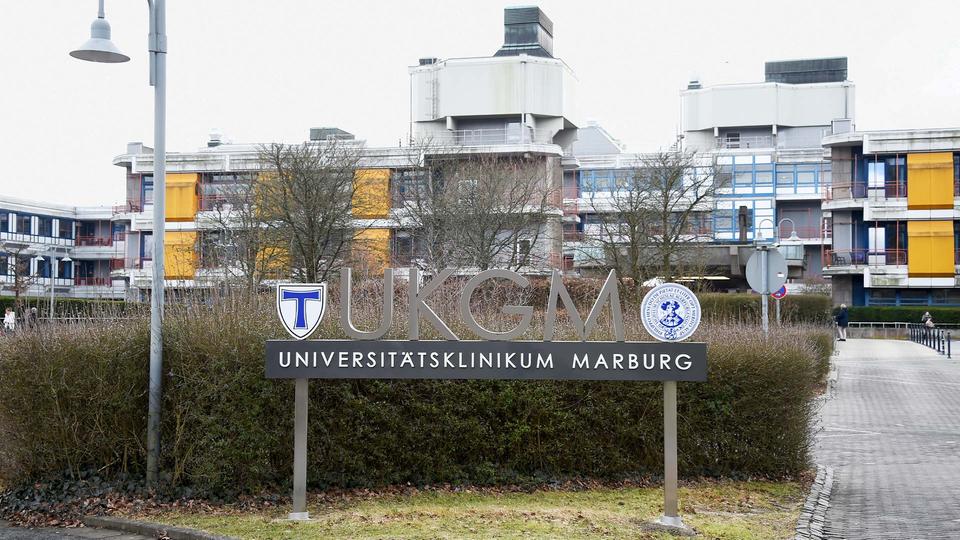 Außenansicht des Gebäudes der Universitätsklinik auf den Marburger Lahnbergen. Im Vordergrund ein Schild auf dem steht "Universitätsklinikum Marburg".
