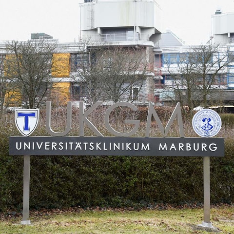 Außenansicht des Gebäudes der Universitätsklinik auf den Marburger Lahnbergen. Im Vordergrund ein Schild auf dem steht "Universitätsklinikum Marburg".