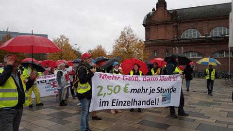 Menschen stehen mit Plakaten und Schirmen vor Hauptbahnhof in Wiesbaden
