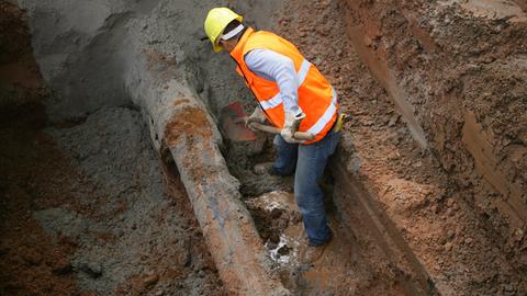 Ein Arbeiter schaufelt in einem Erdloch eine beschädigte Wasserleitung frei.