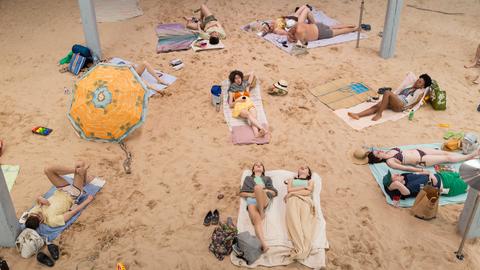 Menschen liegen auf handtüchern an einem Strand.