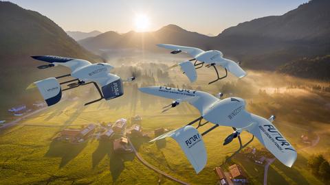Drei fliegende Drohnen des hessischen Start-ups Wingcopter in ländlicher Gegend vor Bergen und Sonnenaufgang