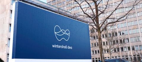 Ein Firmenschild mit dem blau-weißen Logo von Winterhall Dea steht vor dem Bürogebäude der Firma.