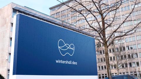 Ein Firmenschild mit dem blau-weißen Logo von Winterhall Dea steht vor dem Bürogebäude des Unternehmens.