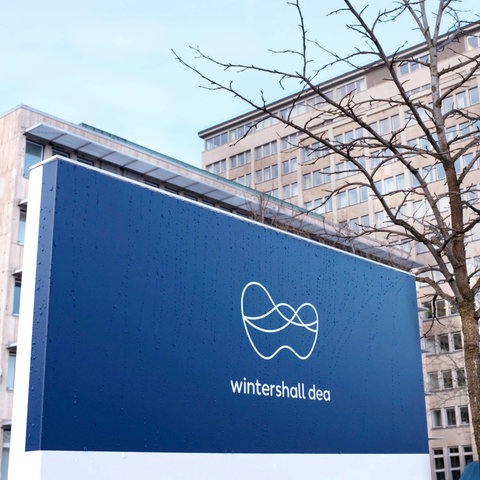 Ein Firmenschild mit dem blau-weißen Logo von Winterhall Dea steht vor dem Bürogebäude der Firma.