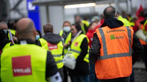Ein Mann kommt während eines Warnstreiks am Flughafen Frankfurt im Oktober 2021 beim Bodenverkehrsdienstleister WISAG mit einer Weste mit "Loadmaster WISAG"-Aufdruck zu seinen Kollegen. 